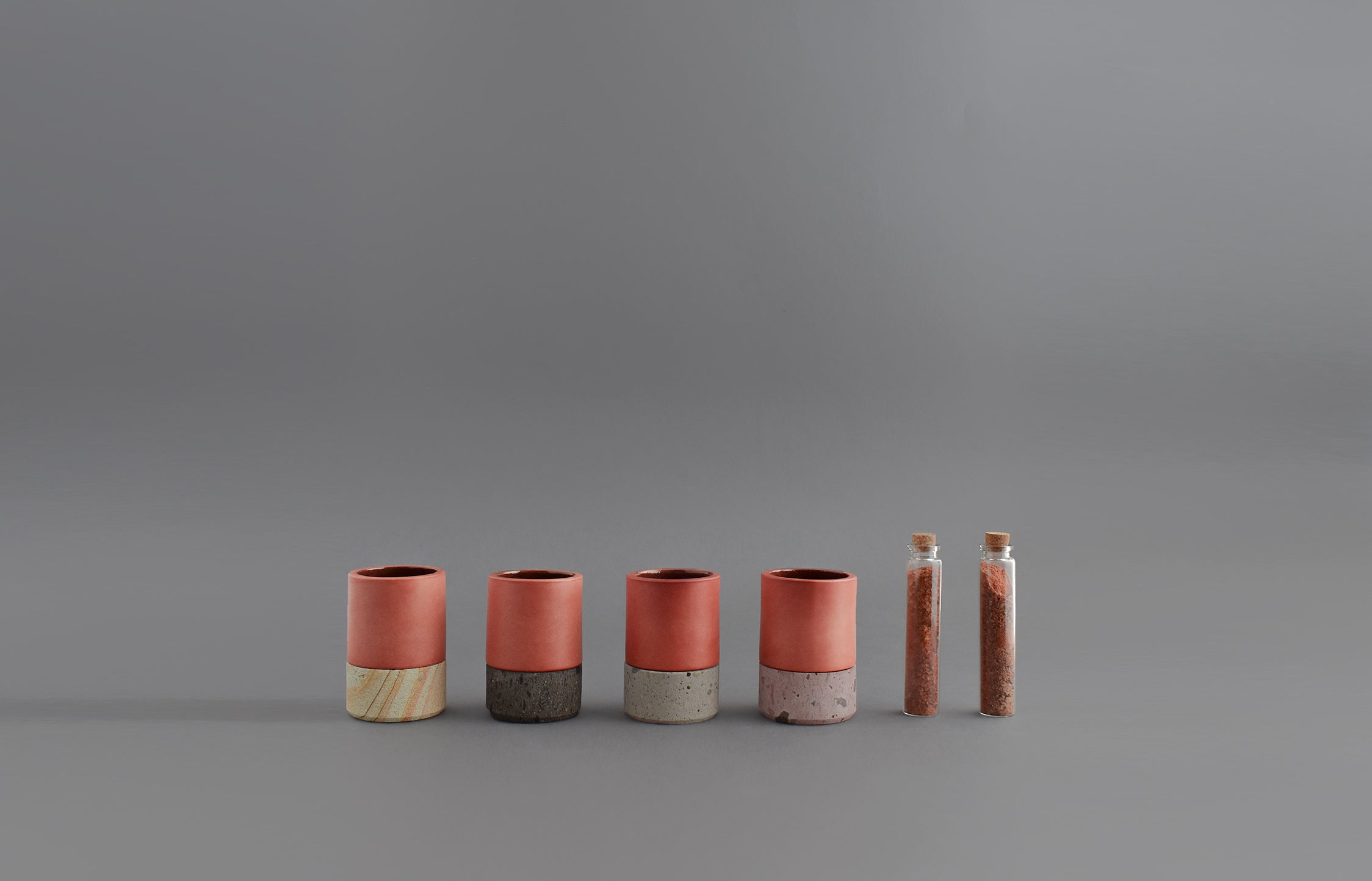 Cuatro vasos mezcaleros de barro con bases de cantera en diferentes colores junto a dos sales de gusano